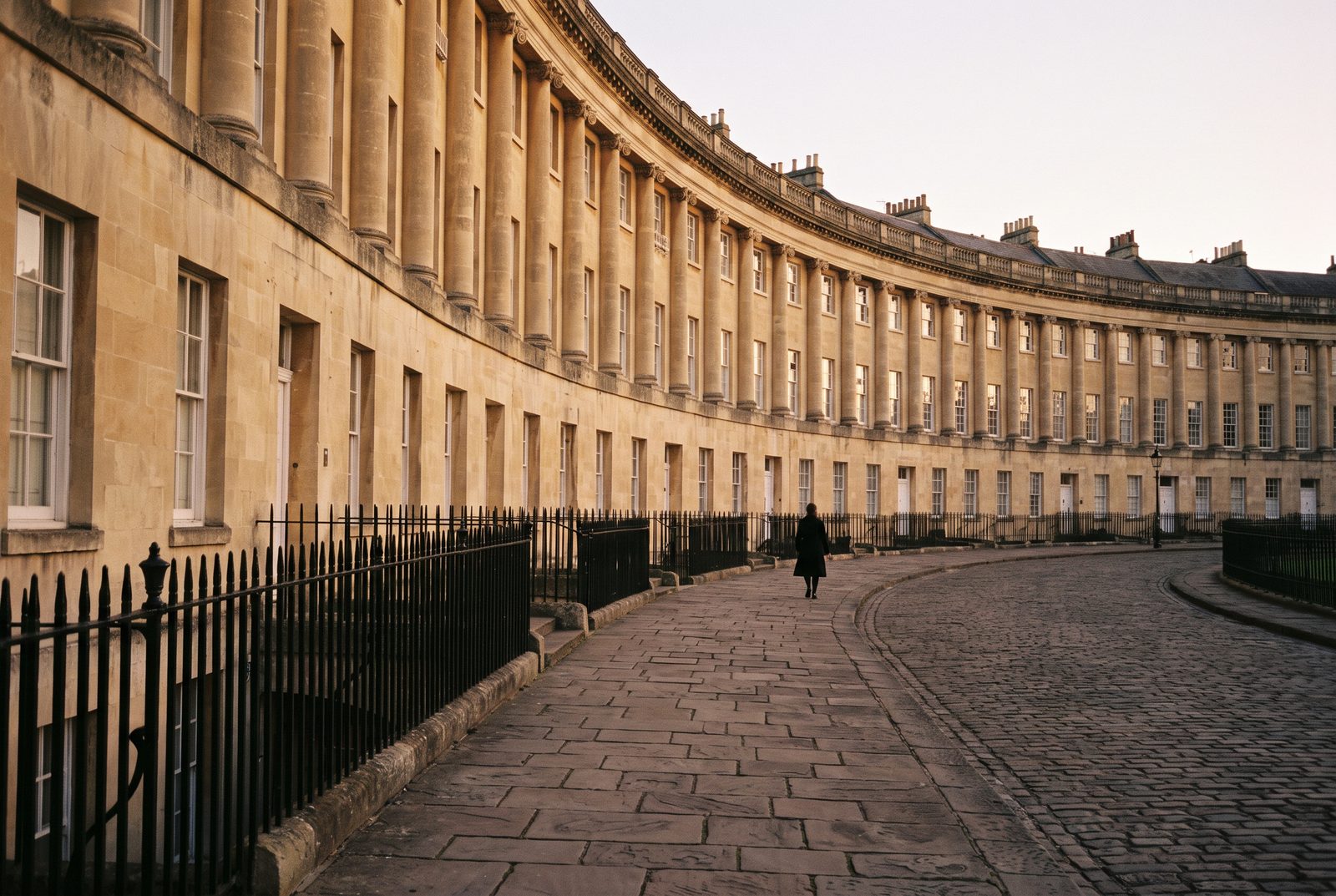 A Georgian crescent in Bath at street level, honey stone in evening light